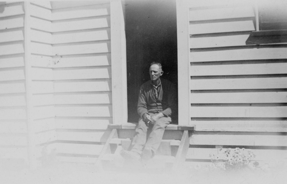 Man Sitting on Doorstep of Wooden House