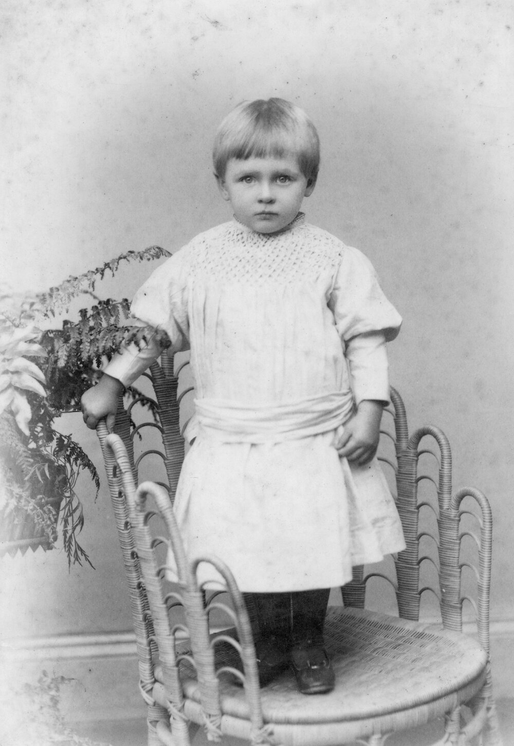 Studio Portrait of Child Standing on Wicker Chair