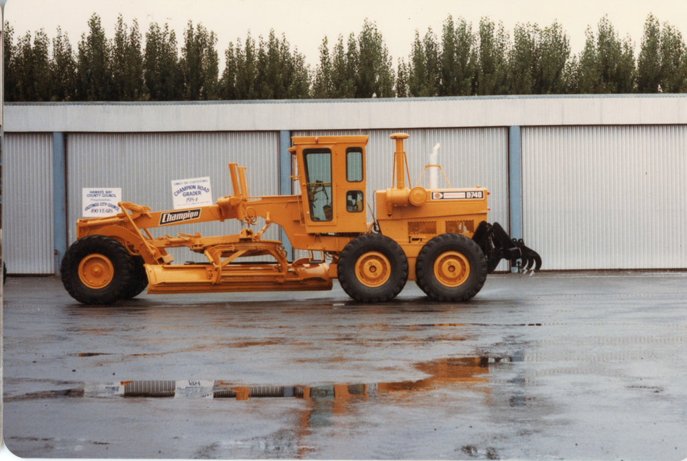 Champion Road Grader Beside Sheds