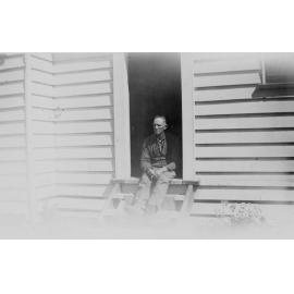 Man Sitting on Doorstep of Wooden House